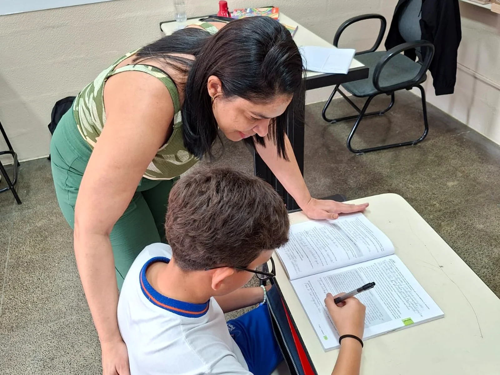 Educadora orientando um aluno durante uma atividade com livro.